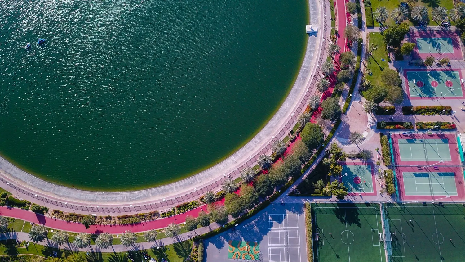 A Dubai park with tennis and basketball courts beside a lake