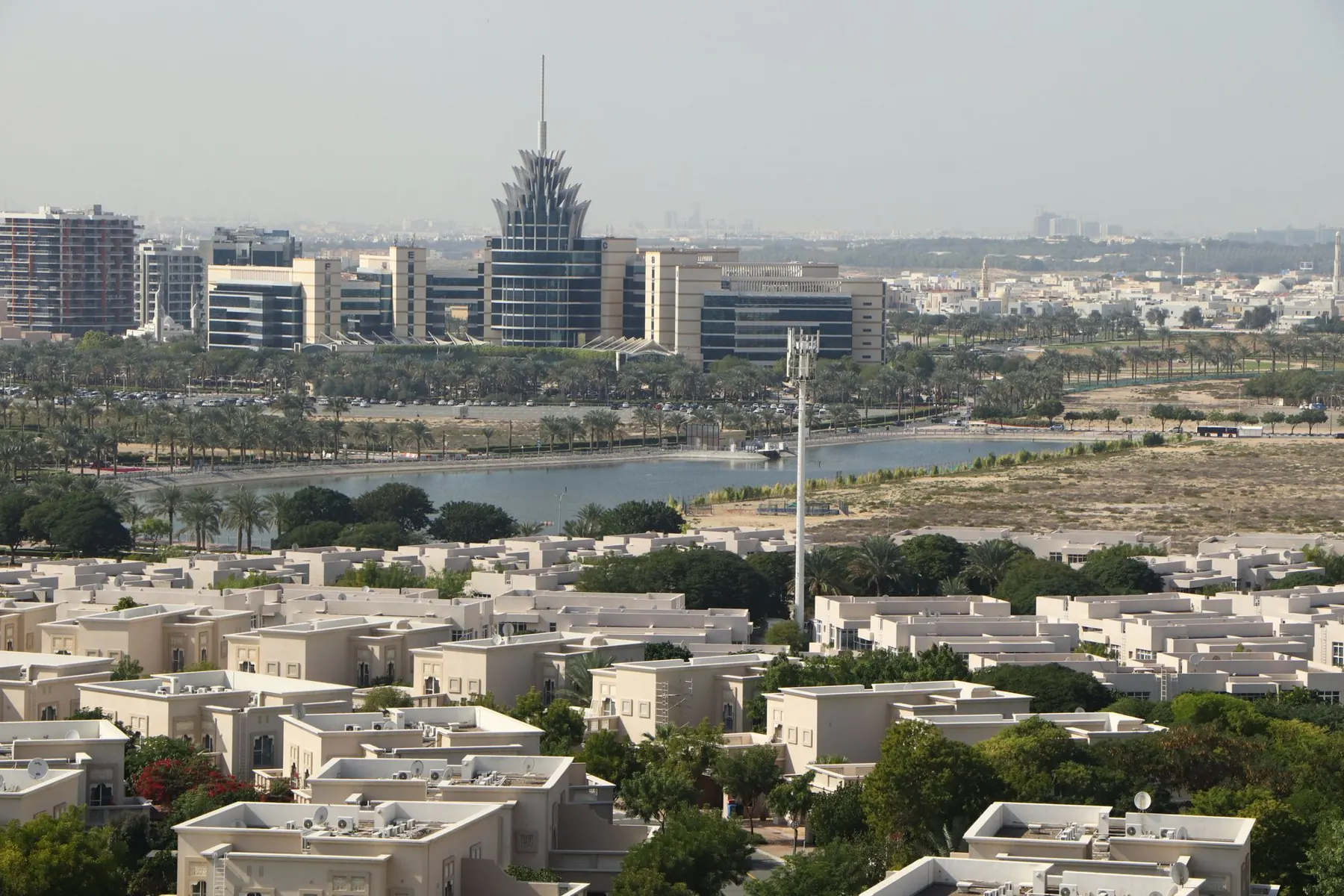 Aerial view across low-rise villas and greenery in Dubai Silicon Oasis, with the DSO headquarters and lake beyond