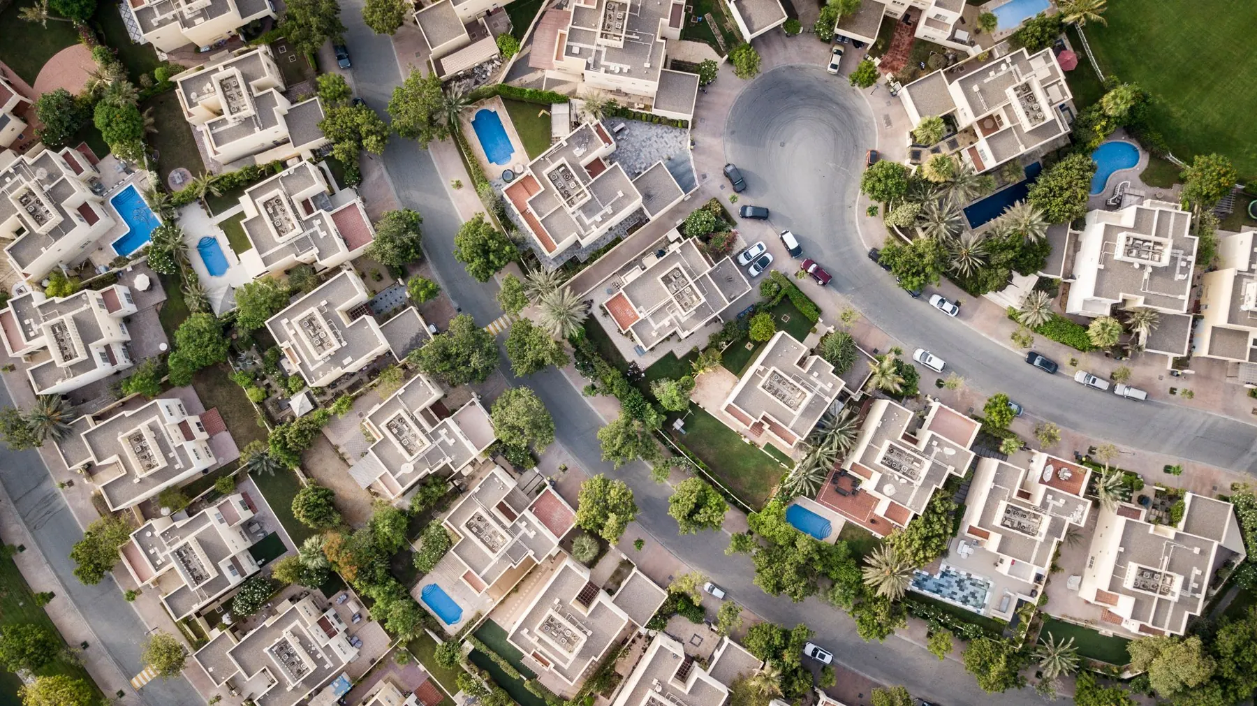 Aerial view over a leafy Dubai villa community with private pools among the trees