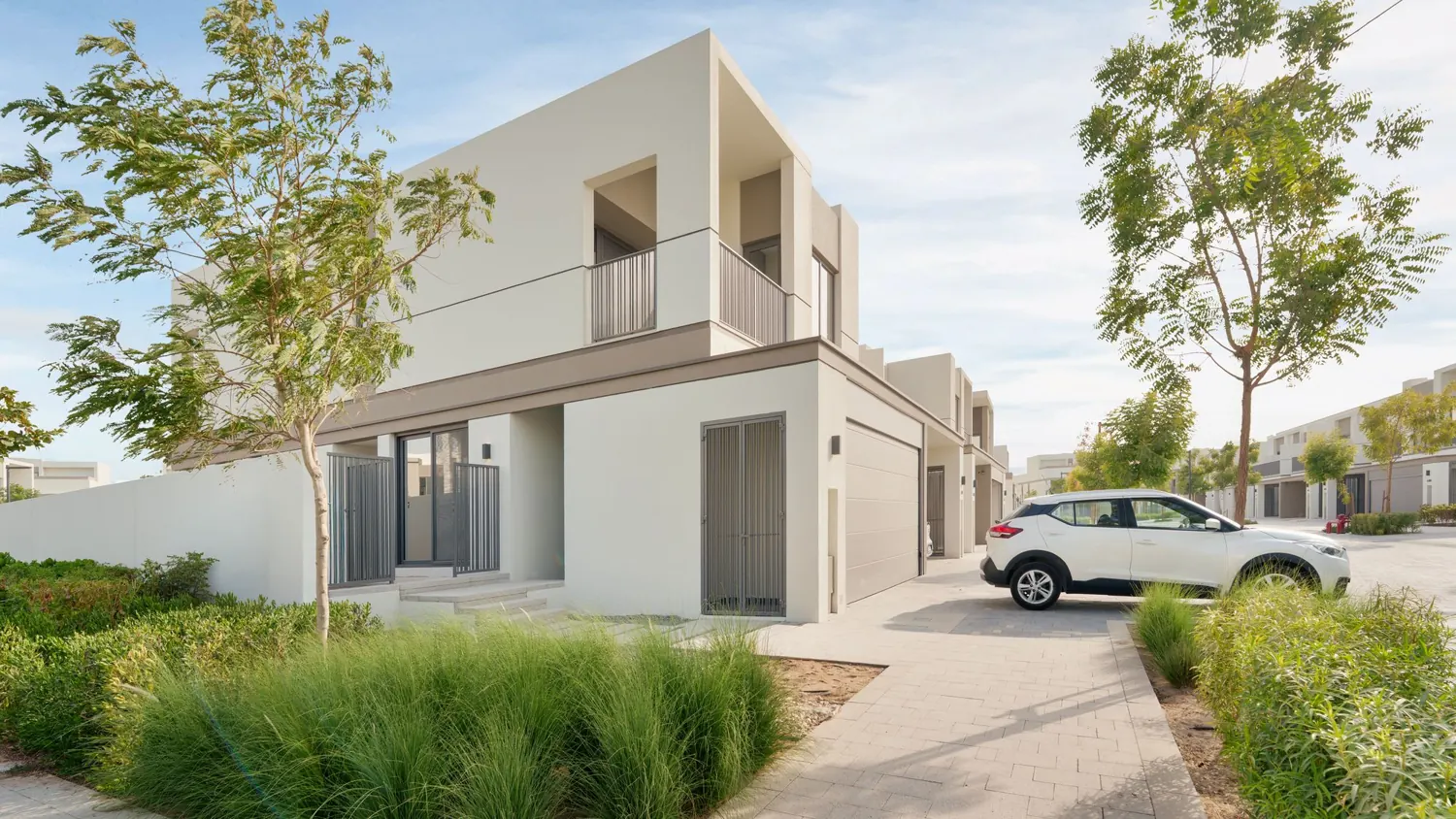 A contemporary white villa behind ornamental grasses and young trees on a quiet Dubai street